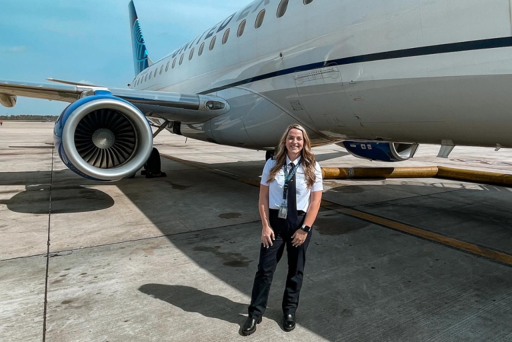 Woman standing and smiling in front of an airplane.