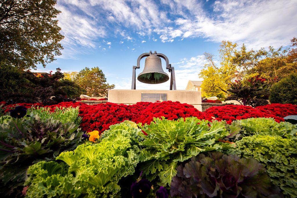 Image of the Founder's Day Bell on the Quad behind blooming flowers and plants.