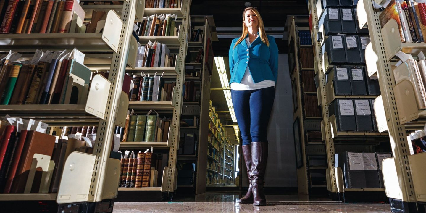 Dr. Katherine Ellison posing between rows of books in a library