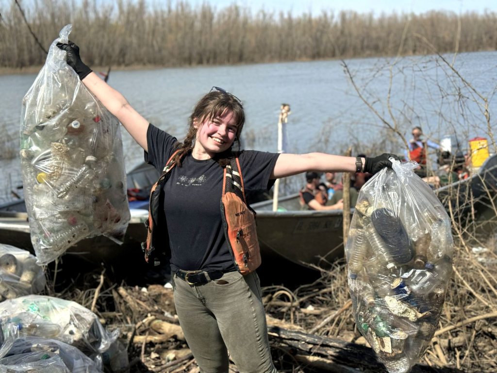 Individual holds two full trash bags in the air while smiling