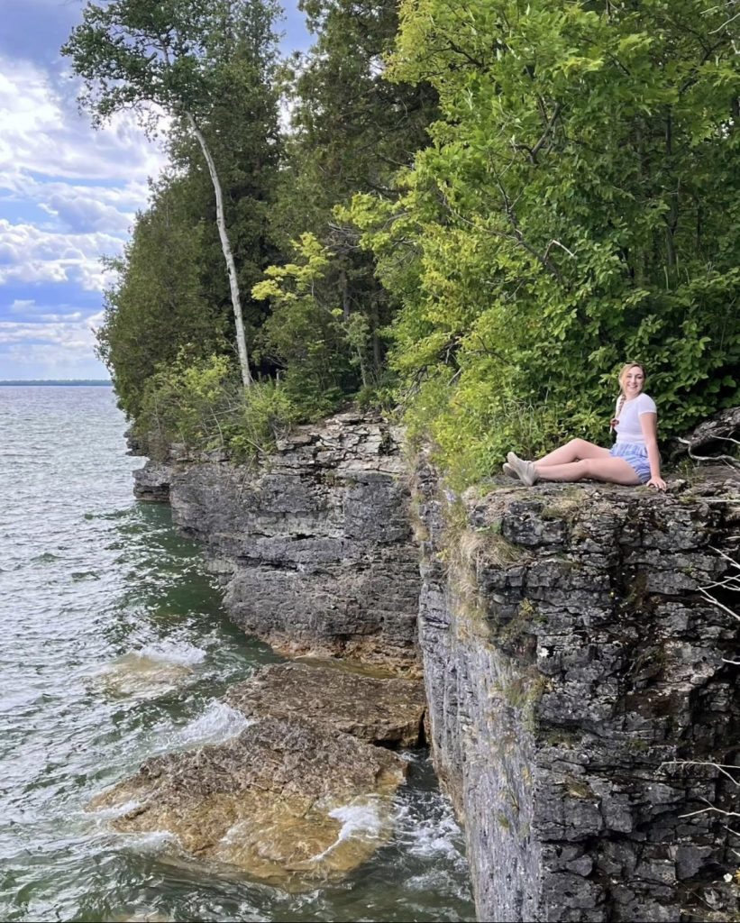 Aleena sitting on a cliff overlooking a lake. 