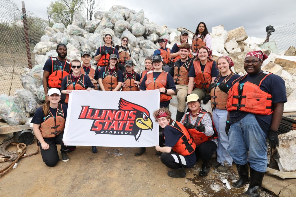 group of students wearing life jackets standing in front of a pile of trash on a barge