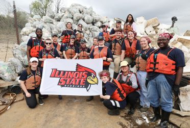 Illinois State volunteers pose for a photo in front of a mountain of trash on the LL&W barge.