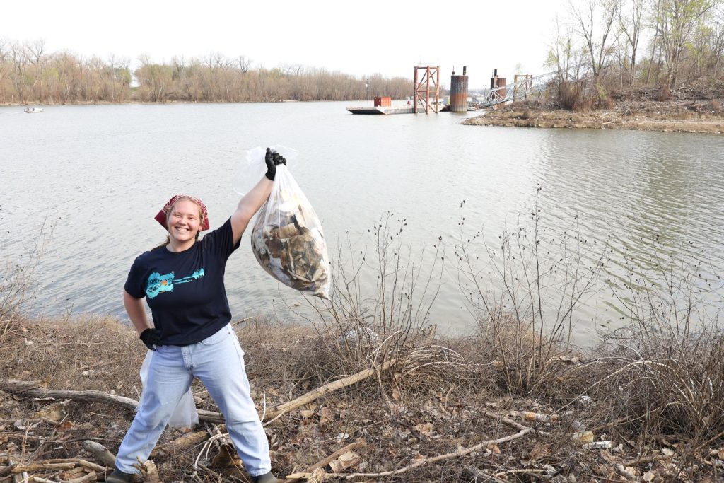Student holding up a bag of trash with a lake in the background