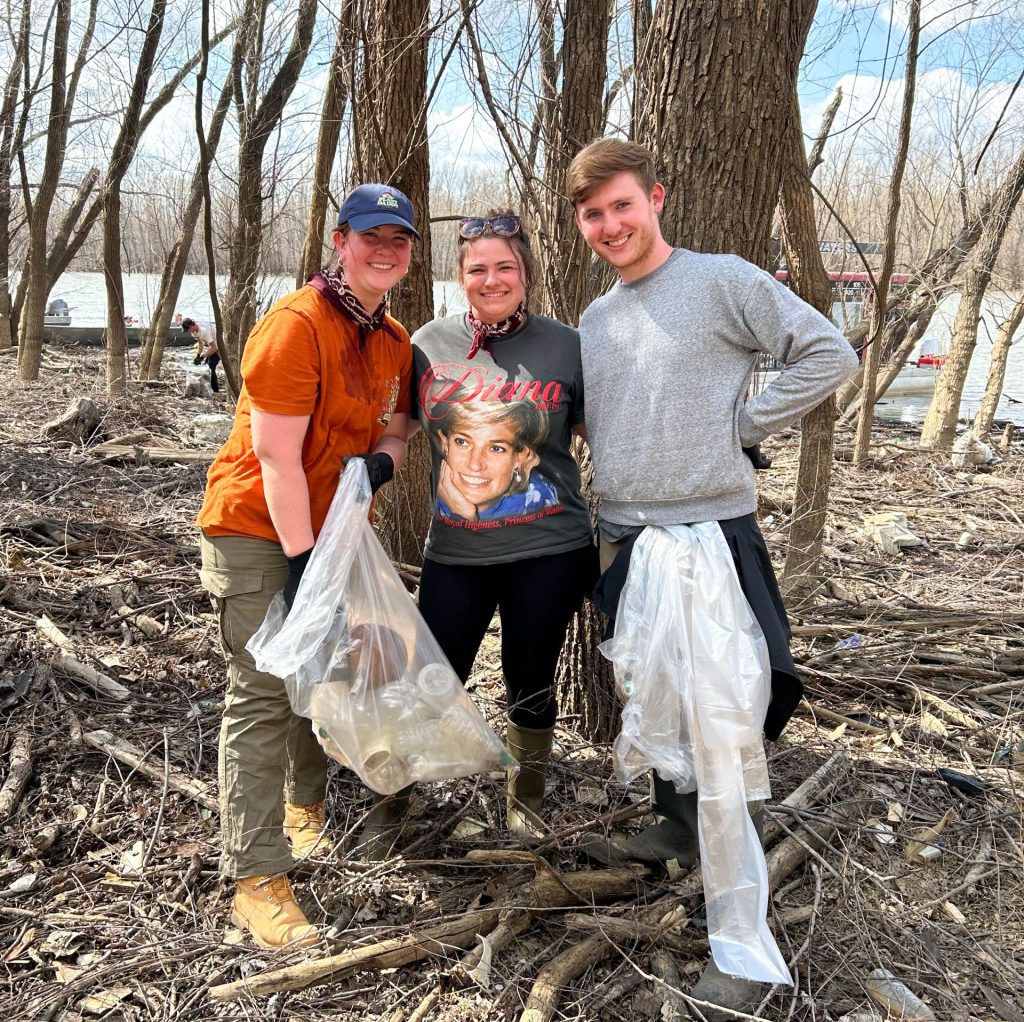 three people posing for a photo holding a bag of trash in the woods