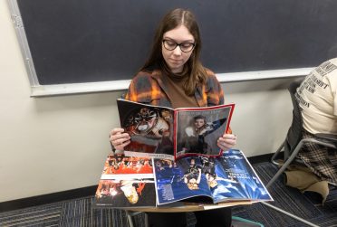 Student sitting at a desk reading a magazine with Taylor Swift on the cover and other magazines featuring Taylor Swift sitting on the desk.