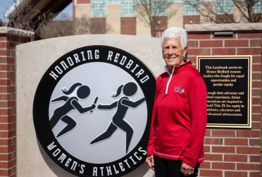 Jill Hutchison standing next to a sign that reads "Honoring Redbird Women's Athletics"