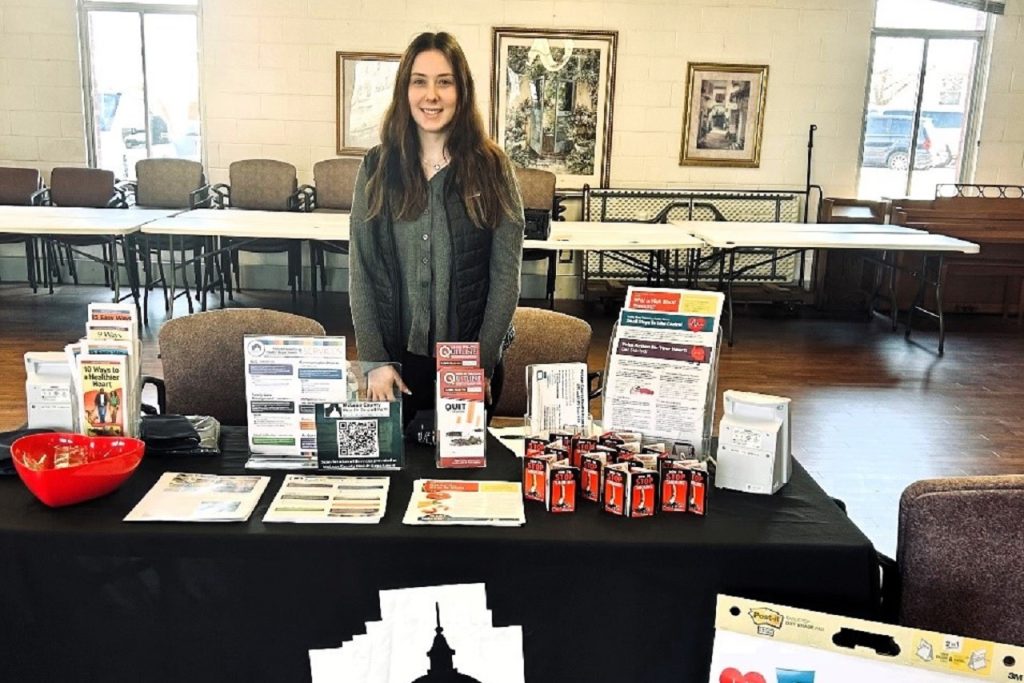 Illinois State University senior Maggie Martyn is seen behind an information table at a heart health event in a residence for older adults as part of her internship with the McLean County Health Department.