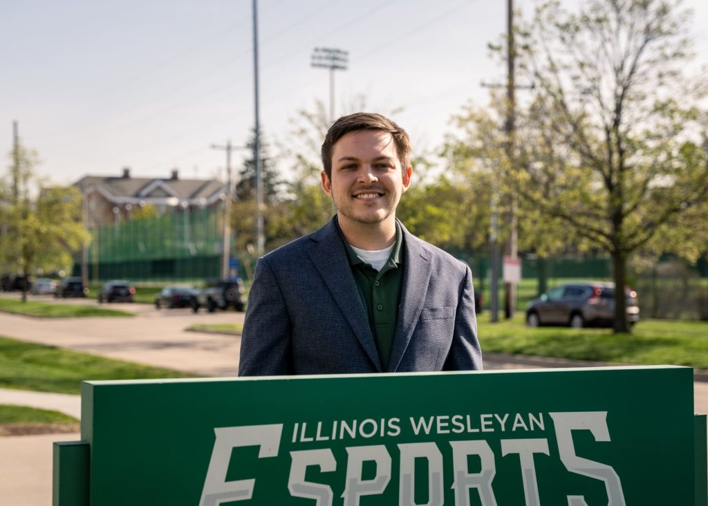 Matt Paliganoff standing behind a sign that reads "Illinois Wesleyan Esports"