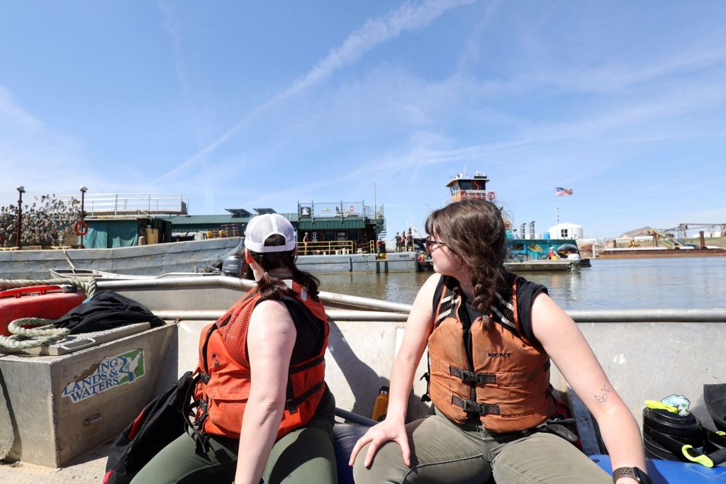 Two people sitting on a boat looking back at a trash barge