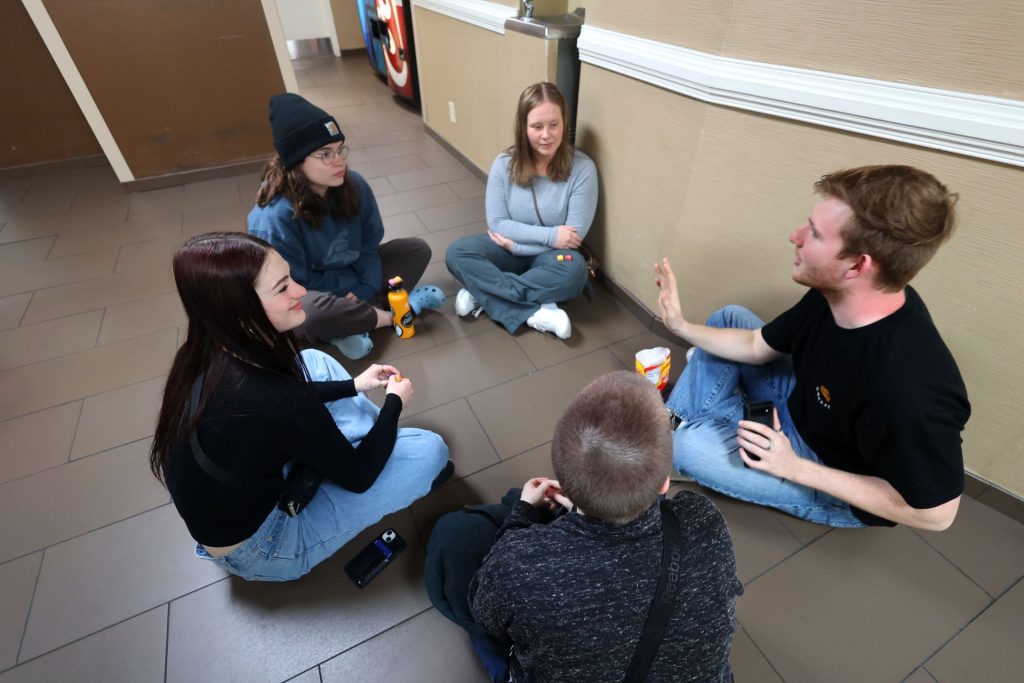 group of five people sit on the floor in a circle talking