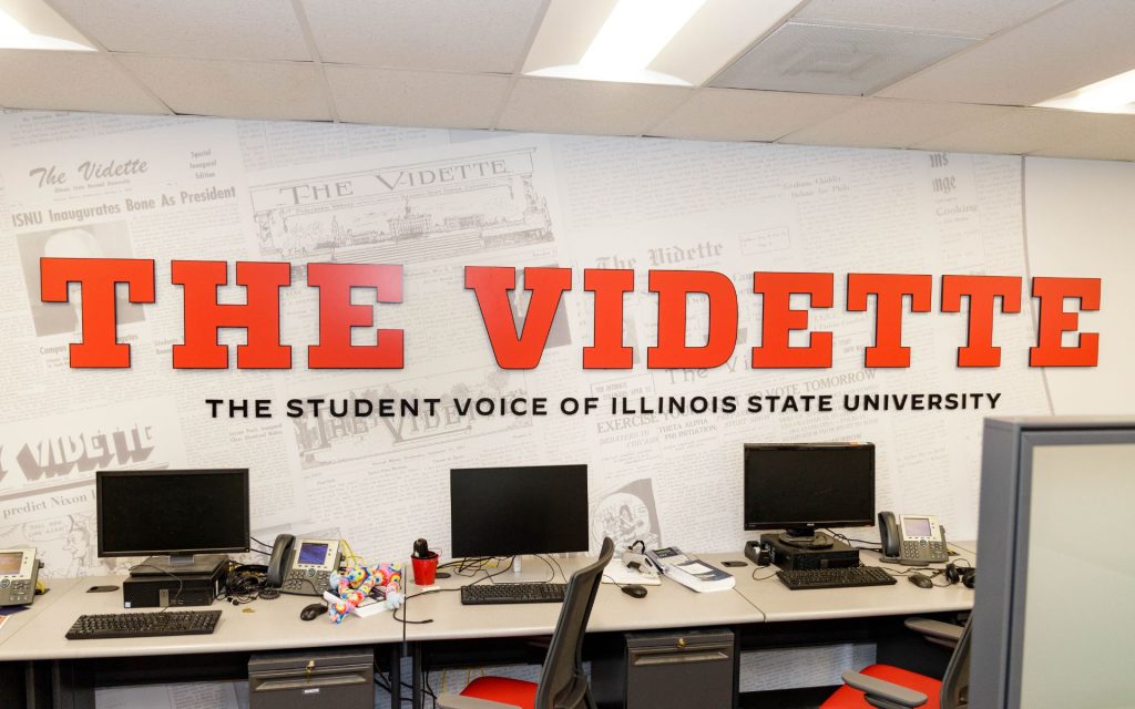 Computers at a desk under a sign that reads "The Vidette"