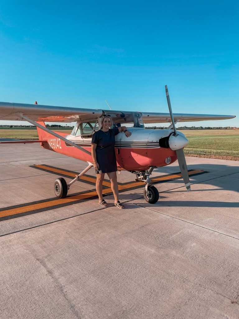 A woman standing next to a small plane and smiling.