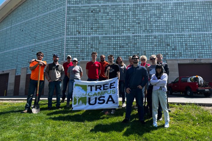 Students standing in front of tree just planted holding a Tree Campus USA banner