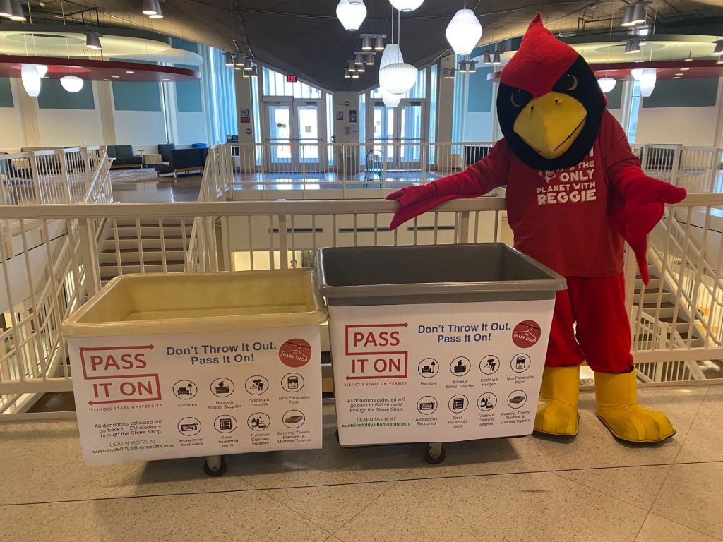 Reggie Redbird mascot stands next to two Pass It On bins.