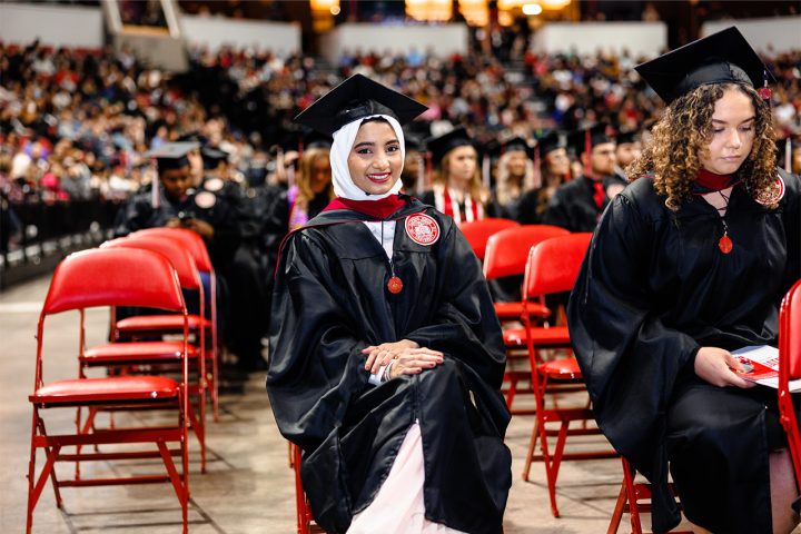 student wearing regalia smiling at the camera from her seat at the Commencement ceremony