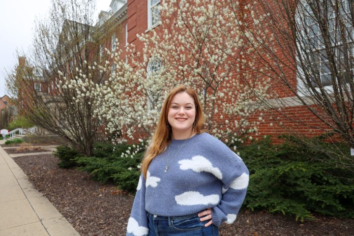 Person stands in front of a brick building and tree with flowers blooming on it