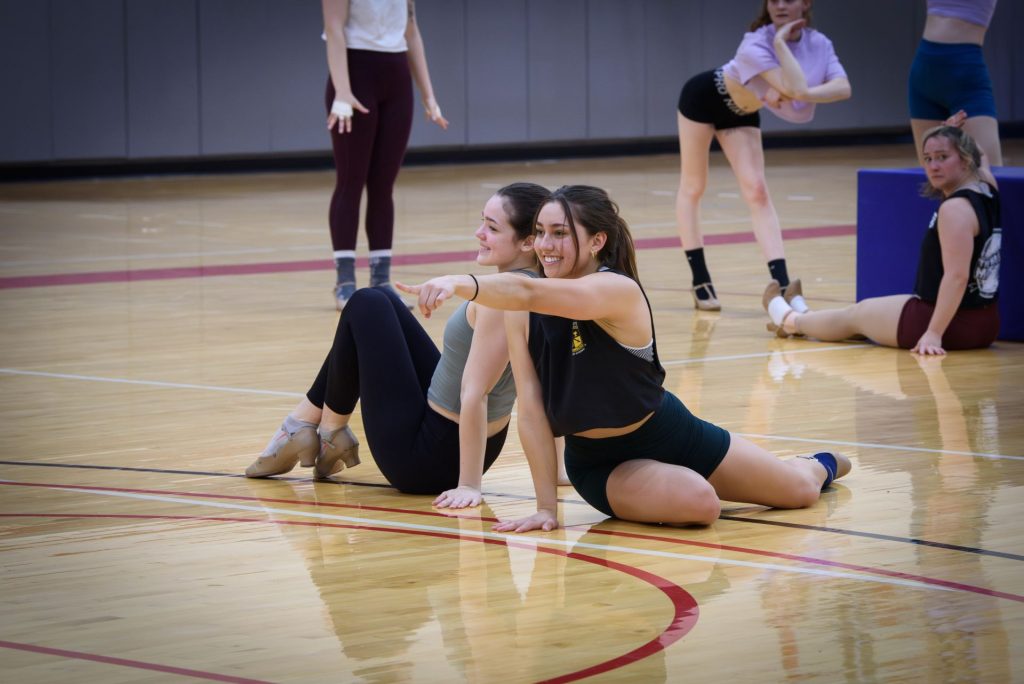 Two Gamma Phi Circus members are on the floor posing and pointing during a dance number.
