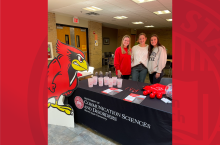 Three CSD students standing at a table during a recruitment event
