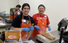 Two people in aprons and hair next sorting pasta at food bank