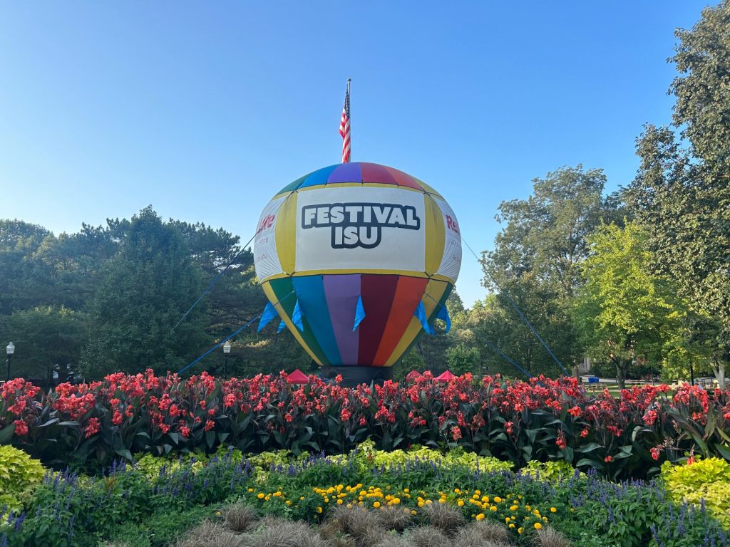Large rainbow colored balloon with words Festival ISU on it sits in a bed of flowers