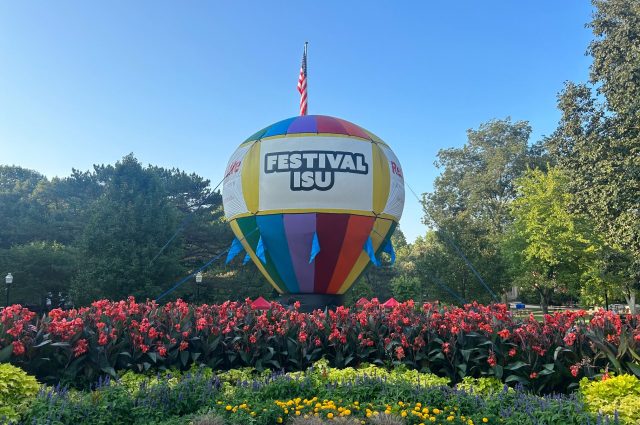 Large rainbow colored balloon with words Festival ISU on it sits in a bed of flowers
