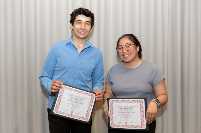 Two students, Michael Severino (left) and Angelica Alvarez (right) pose in front of a curtain with their Triota certificates.