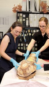 ISU graduate Cailin Meyer, left, works with an intern to examine a child’s iron coffin.