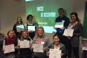 Students pose in front of Voices of Discovery logo
