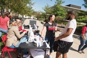 Jennifer Langner explains the free sewing repair service to a student on the Quad.