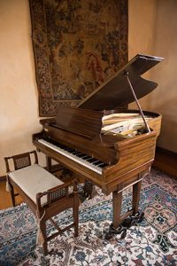 grand piano sitting in the foyer of the Ewing Manor on a rug with a tapestry hanging behind