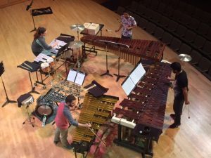Four people playing avariety of percussion instruments on a stage. Shot taken from above them.