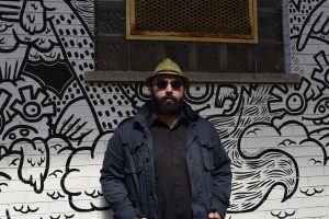 Poet Amish Trivedi stands in front of a mural.