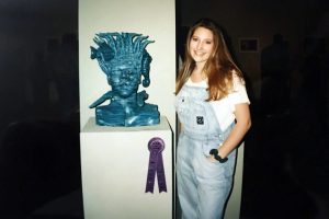 Women standing next to sculpted head bust.