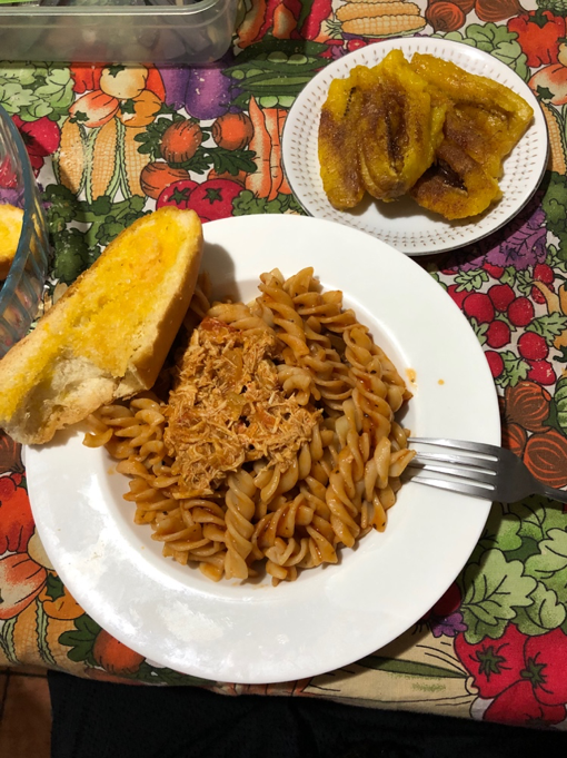 Dinner containing chicken, pasta, garlic bread and plantains topped with brown sugar. 