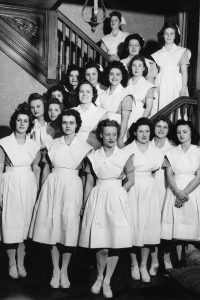 Black and white photo of a housemother with her 17 female nursing students.