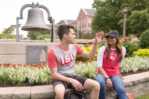 Two students talking while sitting in front of the Old Main Bell