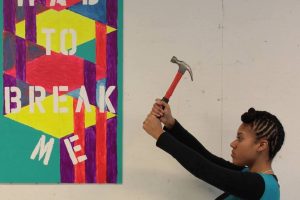 girl holding hammer next to painting