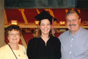 three people smiling, middle person wearing graduation apparel