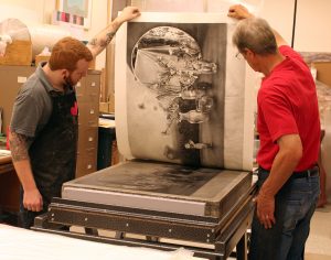 student and faculty pulling a print from a lithographic stone