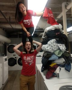 One student standing on another's shoulders next to a pile of laundry 